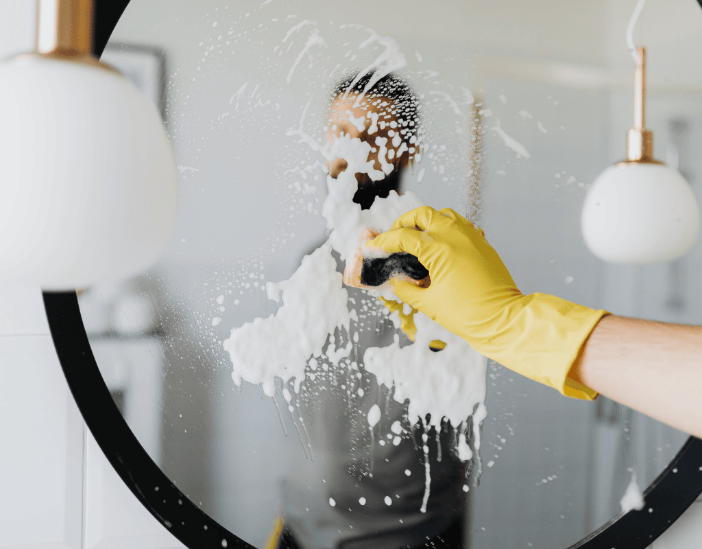 person scrubbing mirror with foam during deep cleaning service